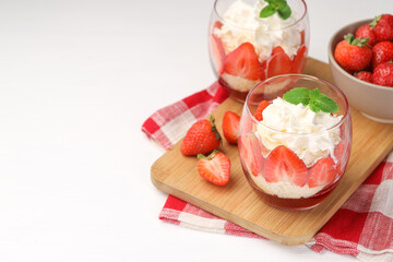Tasty trifle dessert. Sponge cake, strawberries, jam and whipped cream in glasses on white table, space for text