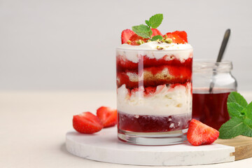Tasty trifle dessert. Strawberries, sponge cake and whipped cream in glass on beige table, space for text