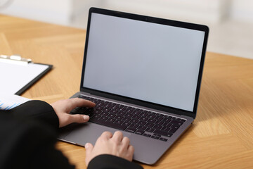 Businesswoman working with laptop at wooden table in office, closeup