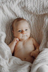 A baby is laying on a blanket with its head resting on its arm. The baby has a smile on its face and its eyes are open. Concept of warmth and comfort