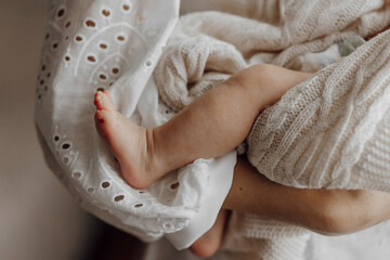 A baby's foot is held in a white blanket. The baby is wearing a white dress