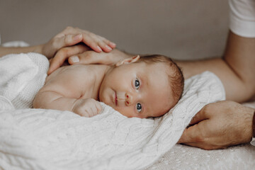 A baby is laying on a blanket with its head resting on a person's shoulder. The baby has blue eyes and a smile on its face. Concept of warmth and love between the baby and the person holding it