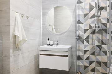 A modern bathroom with stylish geometric tiles, a beautiful circular mirror, functional and elegant