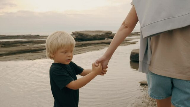 Adorable male child walking seaside resort with mother holding hands with love tenderness slowmo