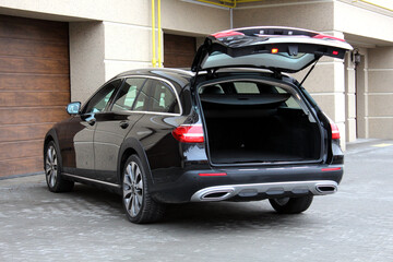 Modern car with open empty trunk outdoors. Black car is ready to load luggage. Clean trunk wagon car. Modern wagon car open trunk. Open back door modern SUV trunk. SUV boot is open. Front view.