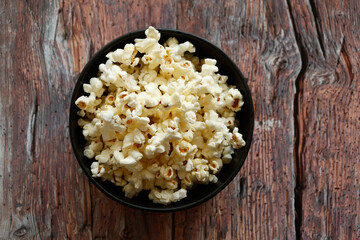 A black bowl filled with freshly popped popcorn placed on a rustic wooden table. 