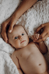 A baby is laying on a blanket with its head resting on a woman's hand. The baby is looking up at...