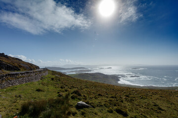 Coastal panorama.  Rolling hills meet a bright, sunny sea.  Islands and waves visible in the distance.