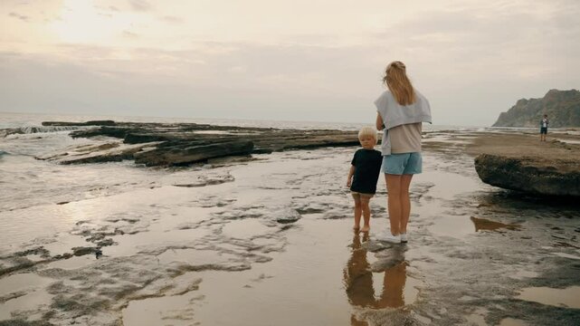 Family summer travel vacation mother father and son walking sea beach with dramatic sky slow motion