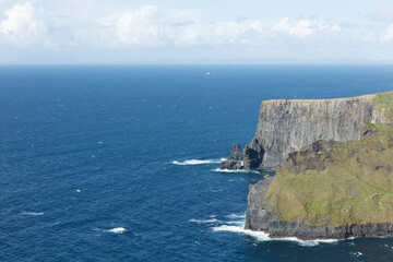 Dramatic cliffs of the Irish coast meet the churning ocean.  Coastal waves crash against basalt rock formations.  Vast expanse of blue water.