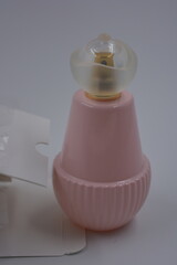 Objects, things, cosmetics and perfumes. A beautiful glass pink bottle with women's perfumes, gold spray and white matte plastic cap is arranged with a white box on a white plastic background.