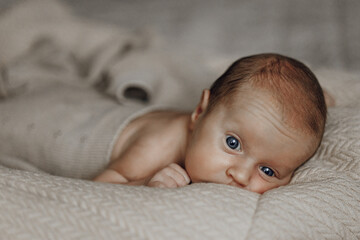 A baby is laying on a bed with a blanket. The baby has blue eyes and a small head