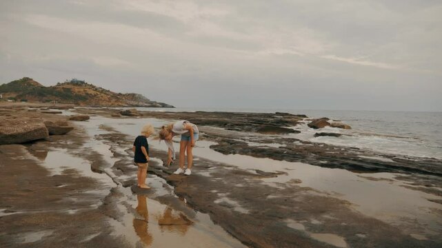 Mother and baby son walking beach together contemplating stone pebble seaside landscape slow motion