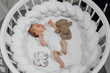 A baby is laying in a crib with a stuffed animal. The crib is surrounded by a white rope