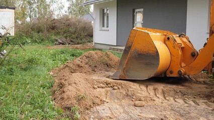 A busy construction site showcasing a digger actively working on landscaping right next to a residential building © bisonov