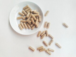 Supplement capsule pills in a small white plate on a white background.