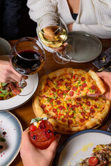 a group of friends holds wine and cocktail in their hands against the background of a table with food