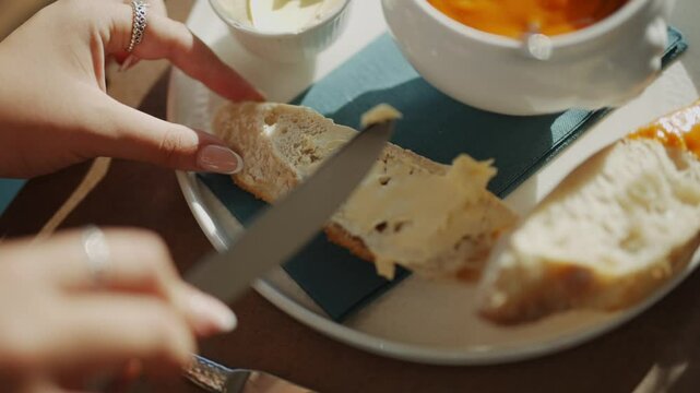 A person is using a knife to cut a piece of bread on a plate. The plate has a slice of bread and a knife on it