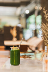 Detox green fresh healthy juice in a glass with straw on table.