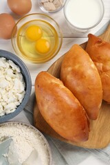 Delicious pirozhki (stuffed pastry pies) and ingredients on white wooden table, flat lay