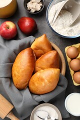 Delicious pirozhki (stuffed pastry pies) and ingredients on grey table, flat lay