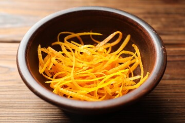 Fresh orange zest in bowl on wooden table, closeup