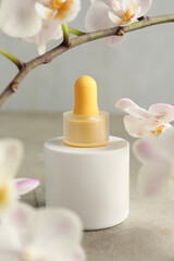 Bottle of skin care product and orchid flowers on gray textured surface