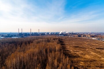 Pm 2.5 industrial concept. Aerial view of an industrial area with smokestacks, surrounded by barren land and sparse trees under a clear blue sky.
