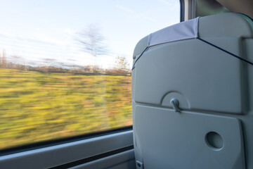 Train journey: The gray backrest of a train seat occupies the foreground, with a blurred landscape...