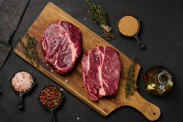 Raw beef steak chuck eye roll on wooden board. Spices for cooking Himalayan salt, peppercorns and thyme sprigs