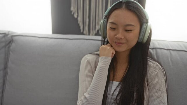Young woman wearing headphones sitting on sofa in living room with a thoughtful expression