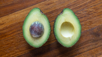 A halved avocado with a pit on a wooden table top view