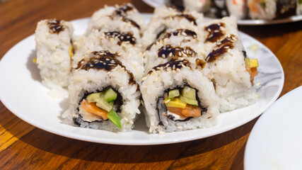 Sliced ​​sushi rolls drizzled with sauce and sprinkled with sesame seeds on a white plate close-up