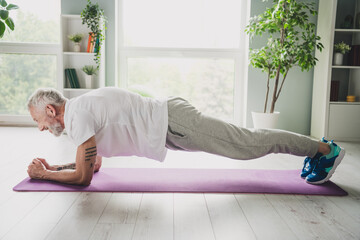 Elderly man practicing a plank exercise on a yoga mat indoors, maintaining fit body with healthy lifestyle