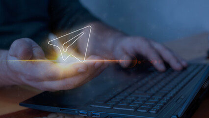 Digital communication concept with glowing paper plane icon in a hand, symbolizing online messaging, file sharing, and innovative technological connection through modern devices like laptops and smart