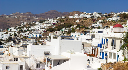 Fototapeta premium Whitewashed buildings of Mykonos town overlooking the Aegean Sea under clear blue sky. Elevated view photography of Cycladic architecture.