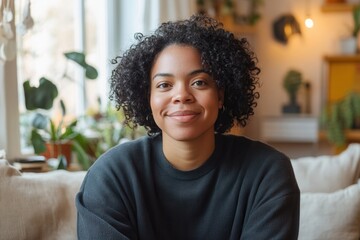 Fototapeta premium Smiling young woman with curly hair sitting comfortably in a cozy living room filled with plants during daylight