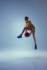 Competitive teenager, basketball athlete jumping in mid air with ball to get powerful slam dunk...