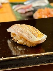 Baby sea bream sushi featuring delicate white and pink flesh on seasoned rice, served on a glossy black plate for an elegant presentation