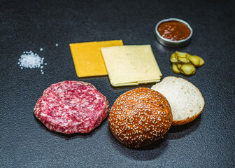 Hamburger ingredients: sesame bun, beef, cheese, onions and red sauce on a dark background.
