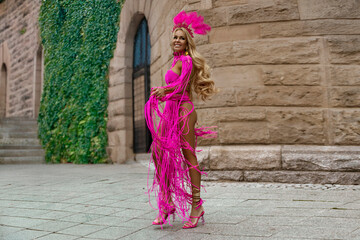 Naklejka premium Sexy blonde model with long legs in sexy pink macramé dress sensually walks around the city on a sunny summer day.