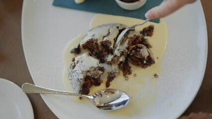 A dessert is being served on a white plate with a spoon. The dessert is a dessert with a white sauce on top