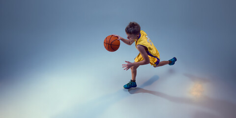 Aerial view of competitive, junior basketball player running and leaping in motion to get goal...