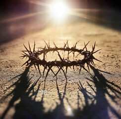 Crown of thorns rests on the ground illuminated by light with a cross in the background, A crown of thorns with the sun shining down on it, casting a shadow on the ground