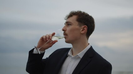 A man in a suit is drinking from a wine glass. Concept of sophistication and elegance, as the man is dressed in a suit and holding a glass of wine. The setting appears to be a formal or upscale event