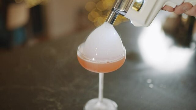 A person is pouring a drink into a glass with a flame. The drink is pink and the flame is blue