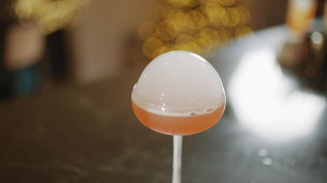 A person is pouring a drink into a glass. The drink is pink and has a foam on top. The person is using a device to pour the drink