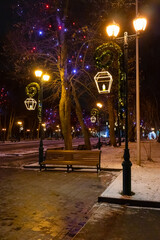 Lampposts and trees in the garden with festive Christmas decorations. Candles on street lampposts and different-colored bulbs on branches in the park