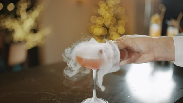 A person is pouring a drink into a martini glass, adding a cherry on top. The drink appears to be a cocktail, and the cherry is floating on top of the liquid