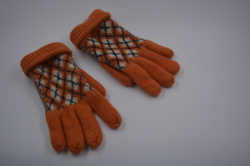 Warm, soft, winter items and household items. Beautiful orange, gray, insulated, knitted gloves are located on a white plastic background.
